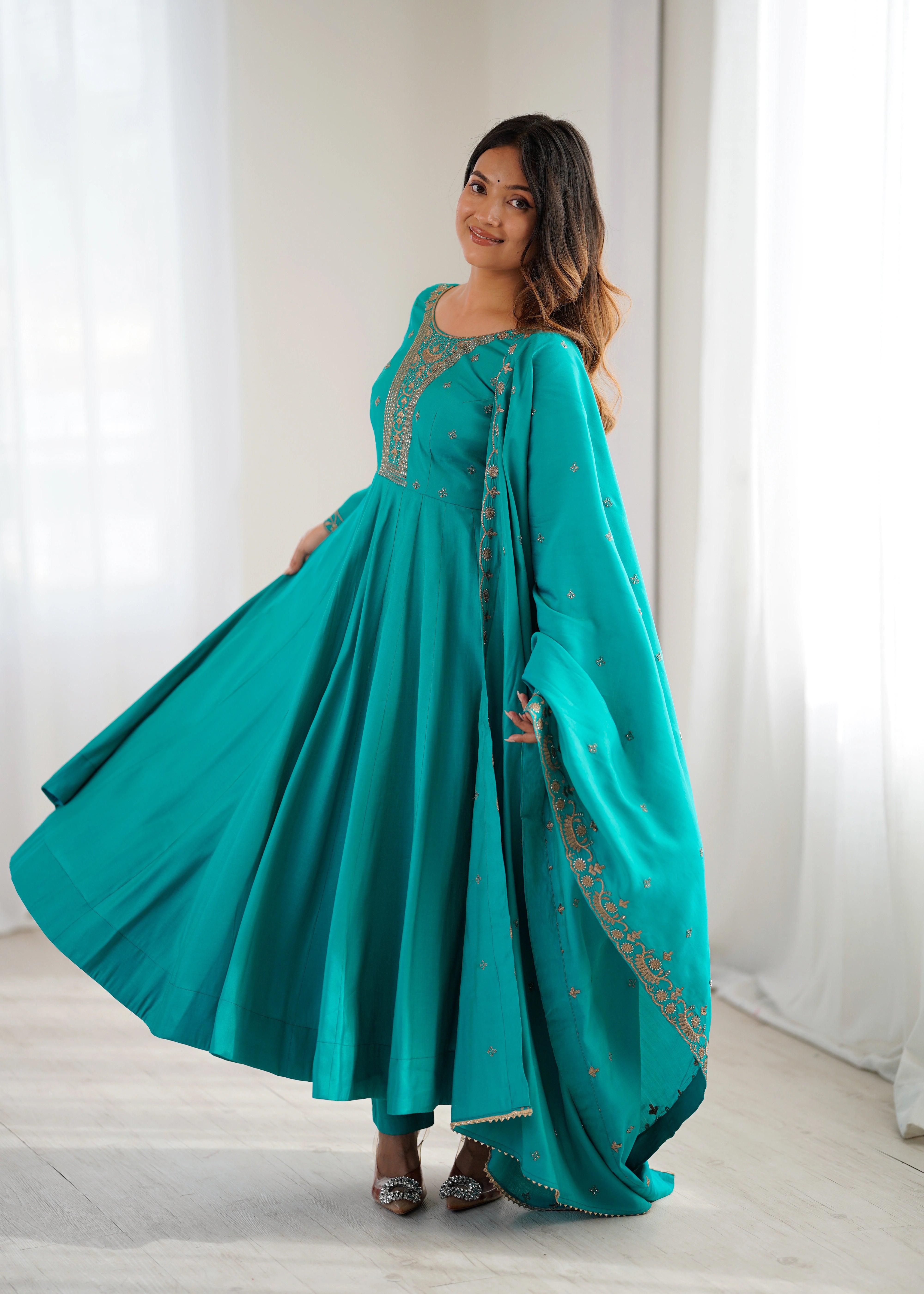 Woman wearing a teal traditional outfit with a matching dupatta against a white curtain background